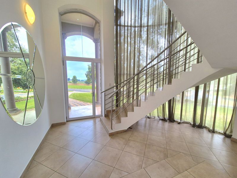 Spacious double-volume entrance hall featuring large glass windows, tiled flooring, and a modern staircase with stainless steel balustrades.