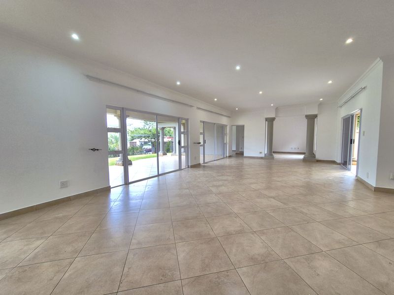 Spacious open-plan living area featuring large sliding glass doors, tiled flooring, recessed downlighting, and decorative structural columns.