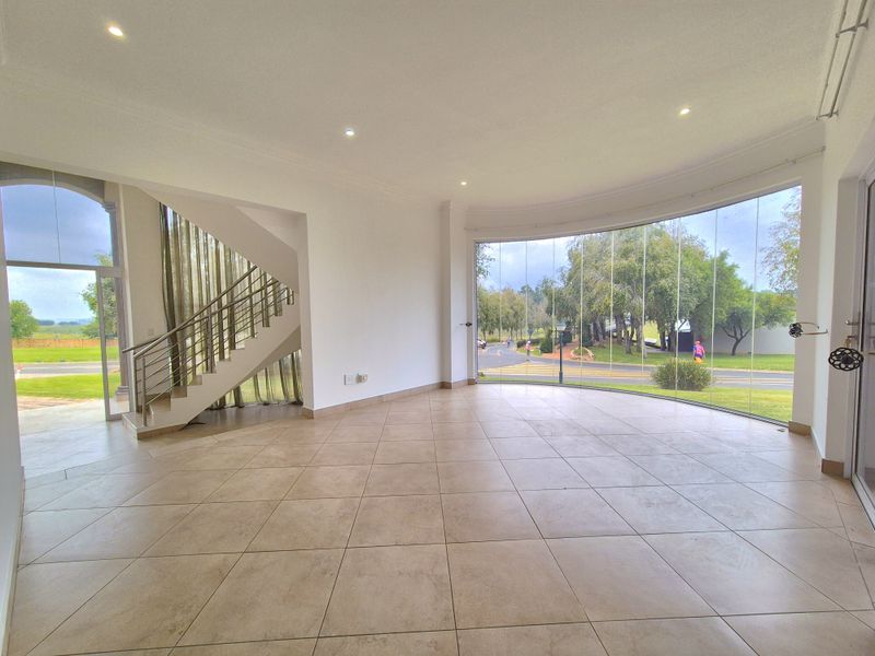 Spacious open-plan living area featuring large floor-to-ceiling glass windows, tiled flooring, and a modern staircase with stainless steel balustrades.