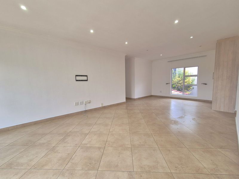 A spacious, empty living area featuring neutral ceramic floor tiles, recessed ceiling lighting, and a built-in storage unit.