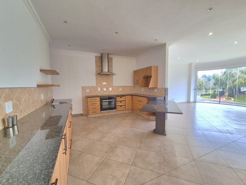 Spacious open-plan kitchen featuring granite countertops, light wood cabinetry, built-in oven, extractor fan, and tiled flooring, flowing into a bright living area.