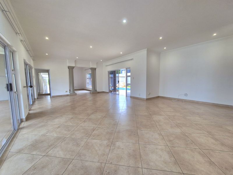 Spacious open-plan living area featuring neutral ceramic floor tiles, recessed downlighting, and sliding glass doors providing access to the outdoor pool area.