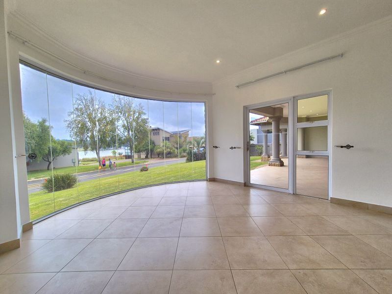 Bright and spacious living area featuring large curved glass windows, tiled flooring, and direct access to an outdoor patio area.