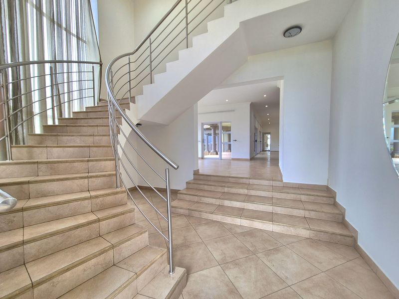 Spacious entrance hall featuring a grand staircase with stainless steel balustrades and tiled flooring, leading into an open-plan living area.