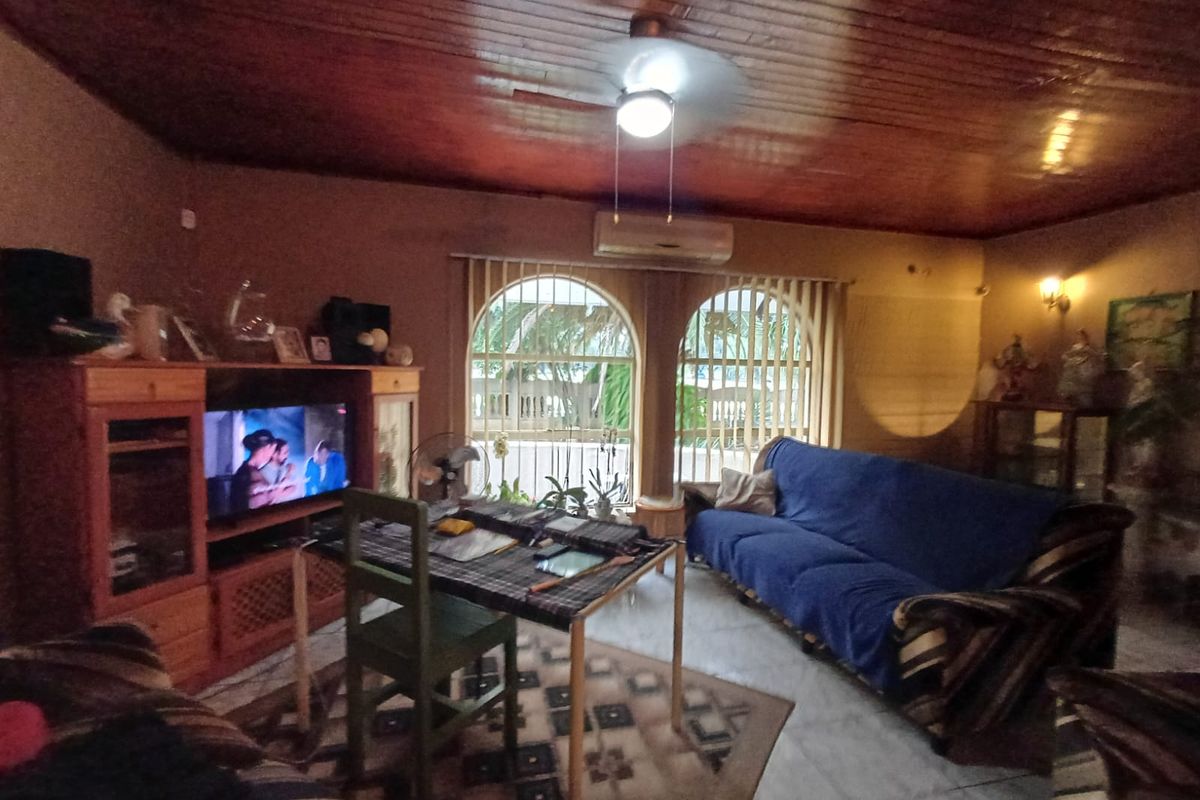 A living room featuring a timber-paneled ceiling, arched windows with security bars, and a wall-mounted air conditioning unit.