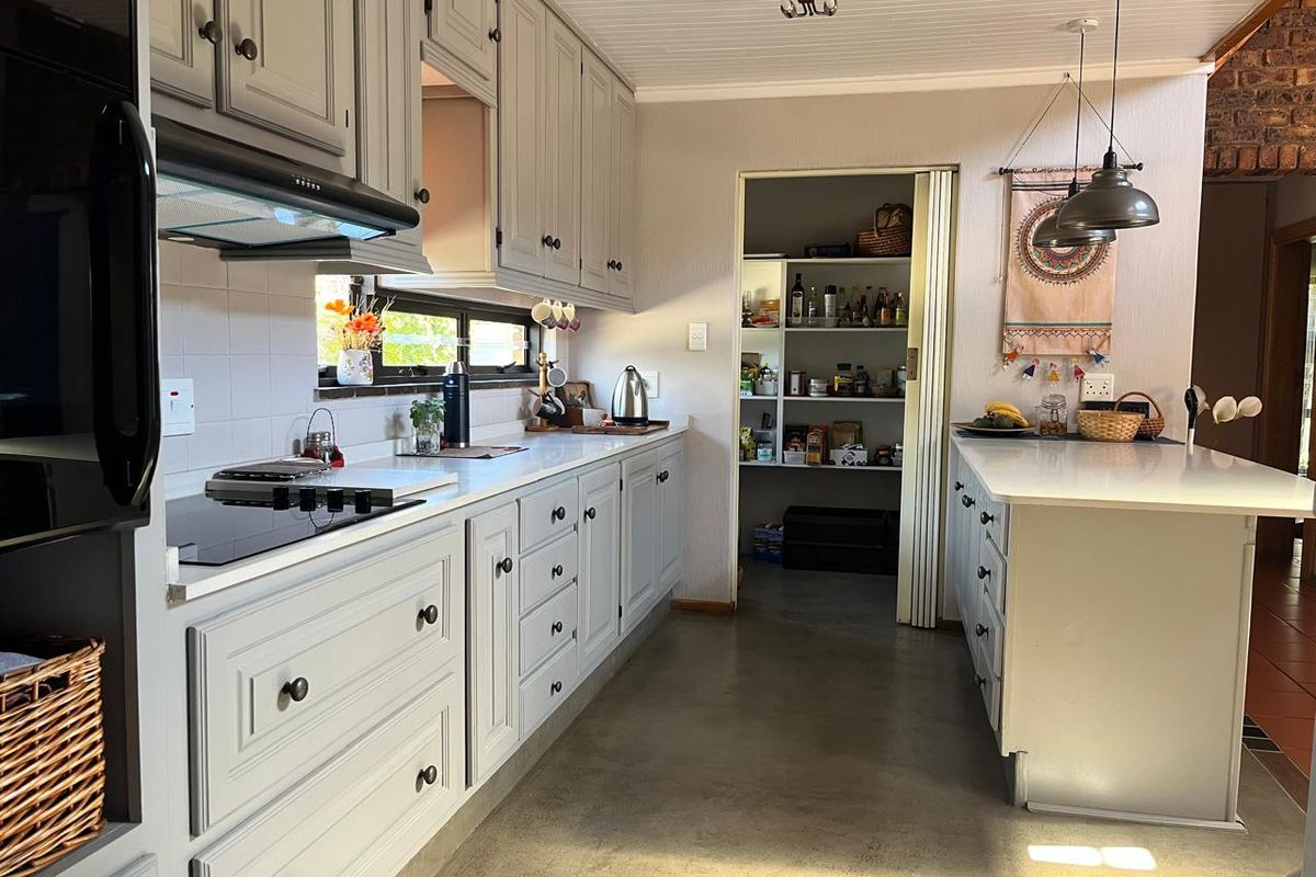 A well-maintained kitchen featuring grey cabinetry, a built-in electric hob, extractor fan, and a convenient walk-in pantry with shelving.