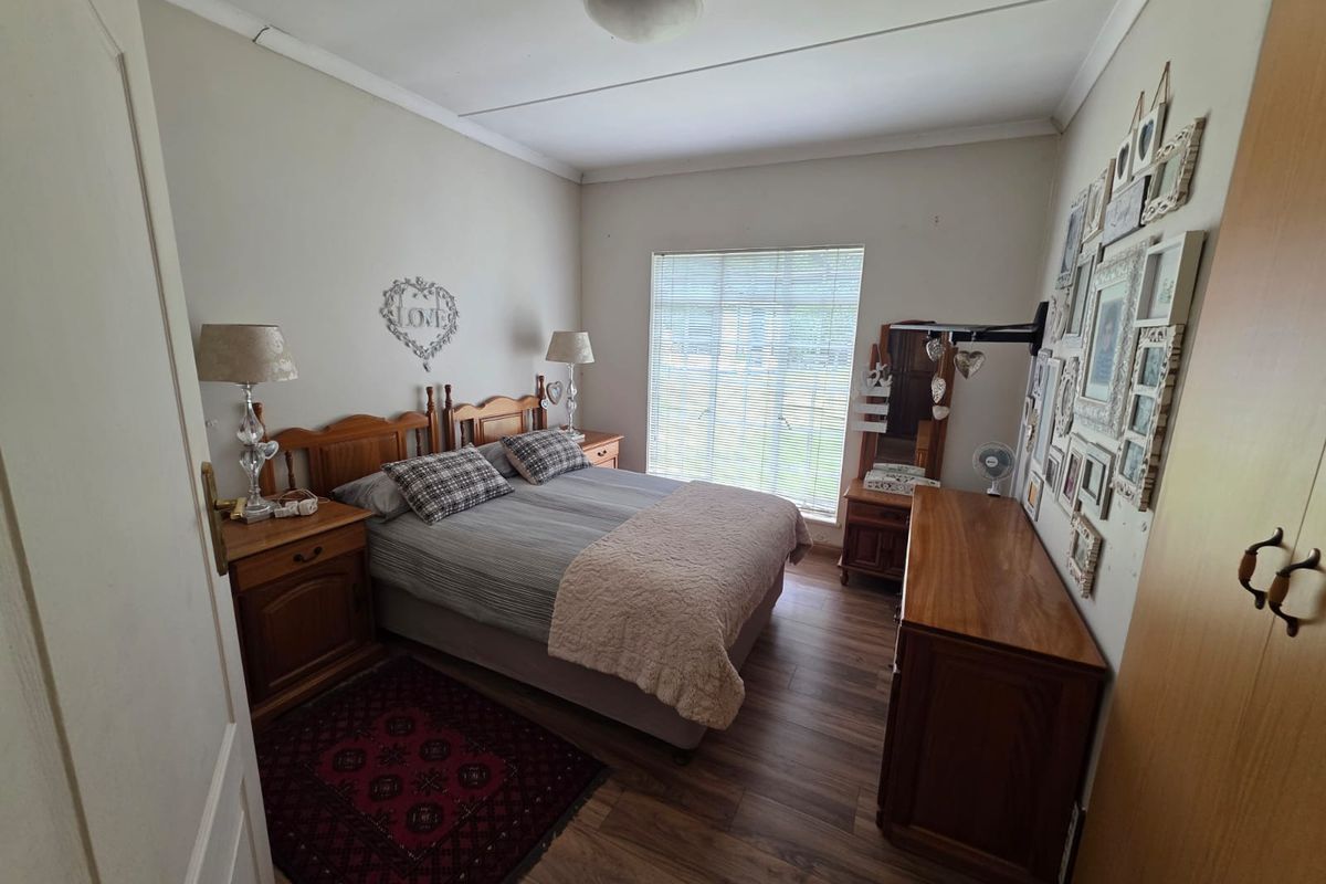 A cozy bedroom featuring wood-look laminate flooring, a large window with blinds, and built-in wooden cabinetry.