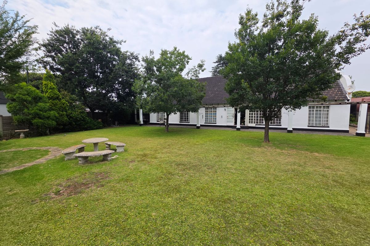 A spacious rear garden featuring a well-maintained lawn, mature trees, and a view of the property's rear facade with white exterior walls.