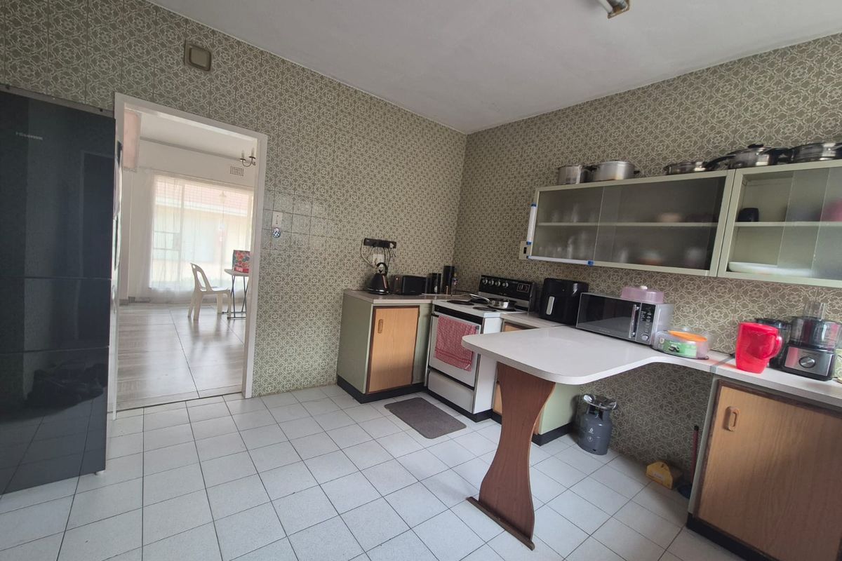 A functional kitchen featuring tiled flooring, built-in cabinetry, and a breakfast counter, with an adjacent view into the living area.