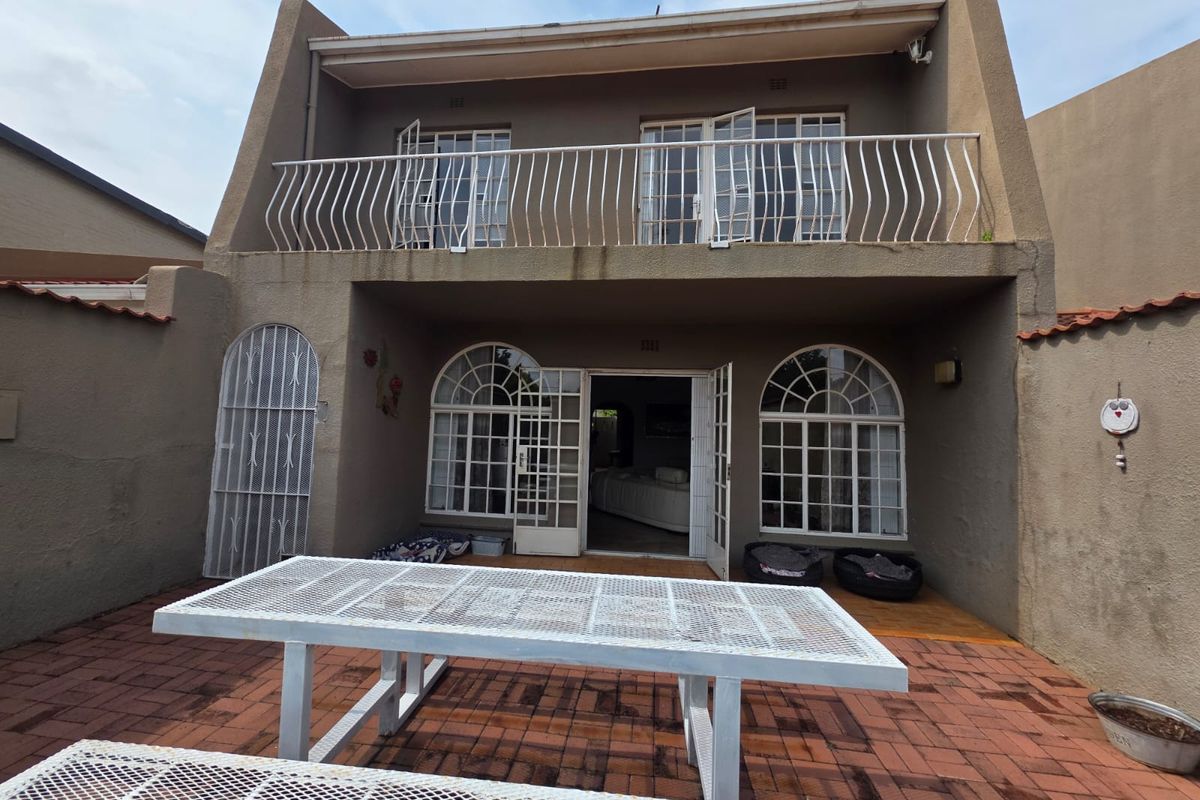 Rear view of a townhouse featuring a paved patio area, ground floor arched glass doors, and an upper-level balcony with metal railings.