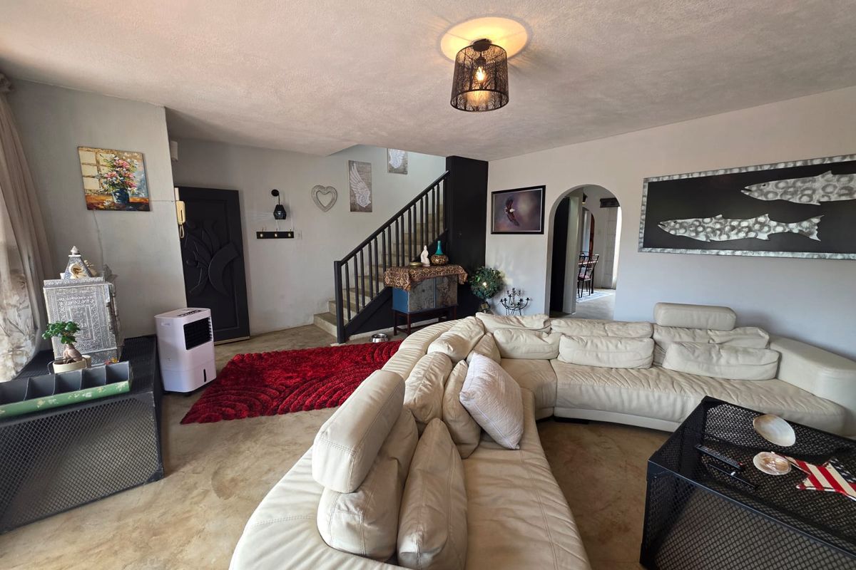 Spacious living area featuring a staircase with a dark wooden balustrade, arched doorway, and polished concrete flooring.