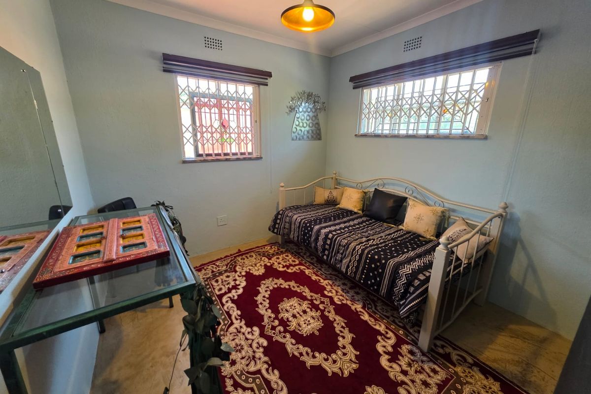 A bedroom featuring light blue walls, security bars on windows, and a central pendant light fixture.