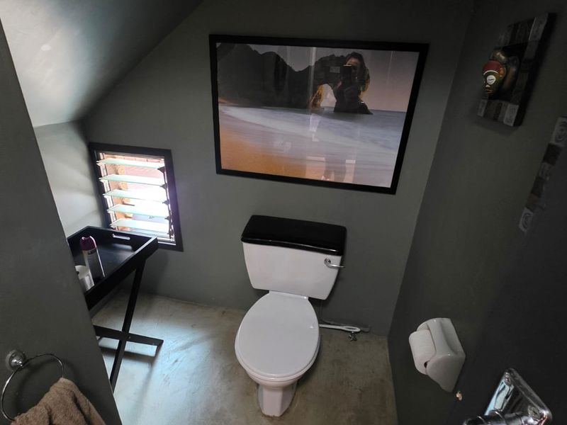 A compact bathroom featuring a toilet, louvre window, and dark-toned walls, providing a functional space with a unique architectural layout.