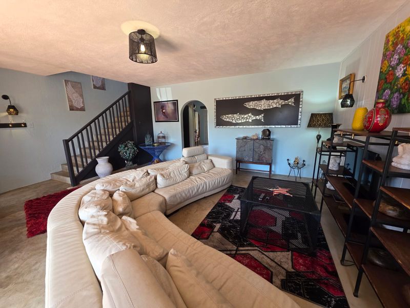 Spacious living room featuring a staircase, arched doorway, and neutral wall finishes, providing a comfortable and functional layout for relaxation.