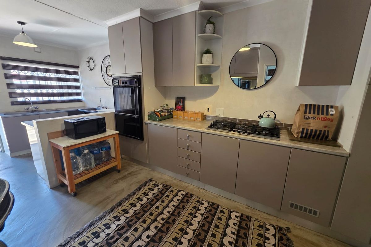 A functional kitchen featuring modern laminate cabinetry, a built-in oven, gas hob, and stone countertops, with an open-plan layout connecting to the adjacent living area.