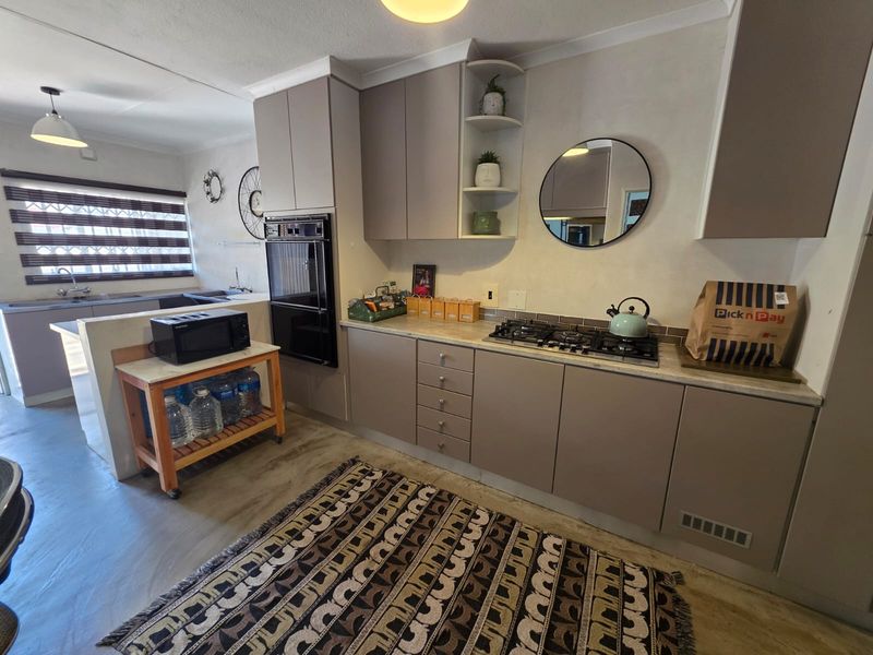 A functional kitchen featuring modern laminate cabinetry, a built-in oven, gas hob, and stone countertops, with an open-plan layout connecting to the adjacent living area.