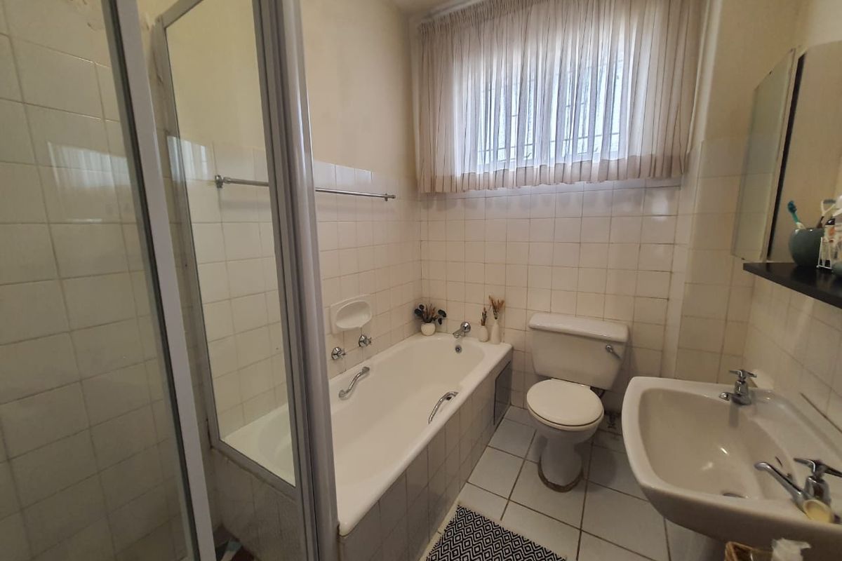 A functional bathroom featuring a built-in bathtub, separate shower enclosure, pedestal basin, and toilet, with classic white wall tiling throughout.