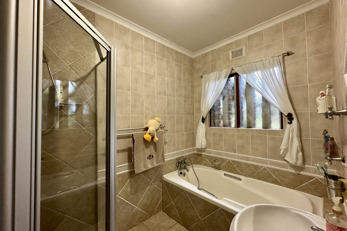A functional bathroom featuring a built-in bathtub, a separate glass-enclosed shower, and neutral wall and floor tiling.
