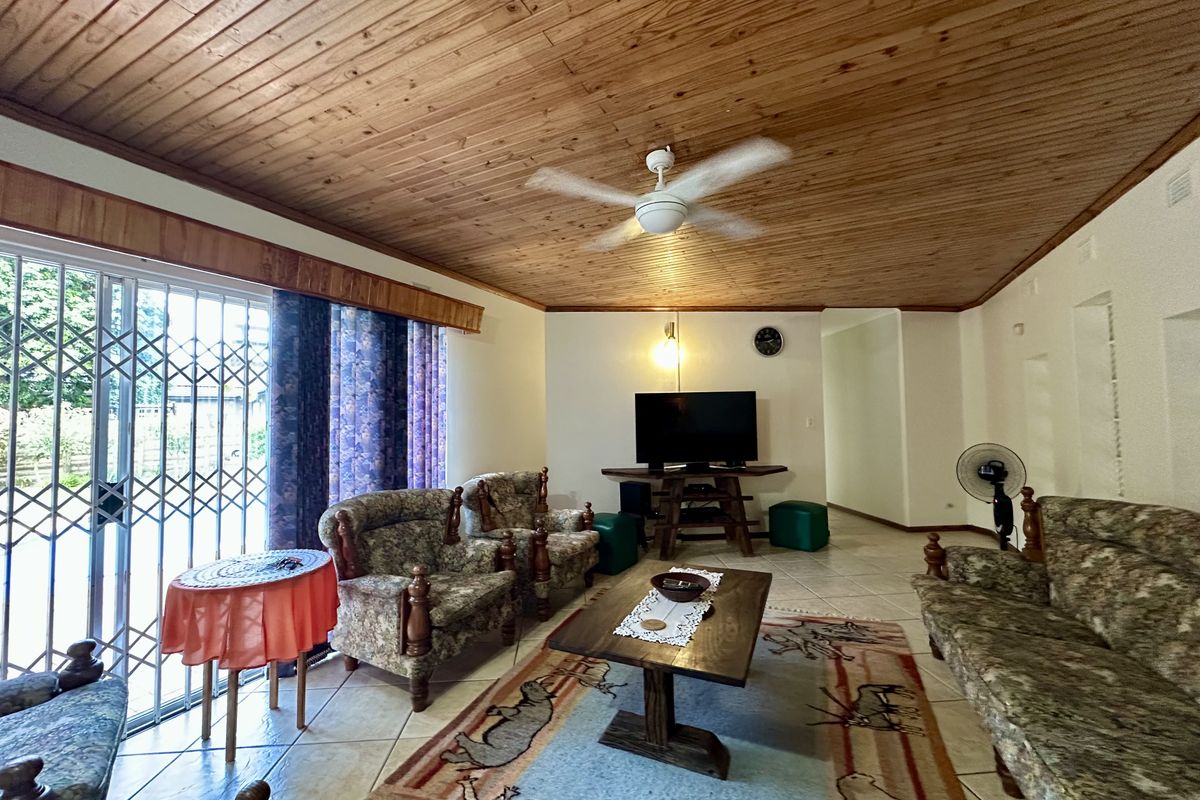 Spacious living room featuring a timber-clad ceiling, ceiling fan, and sliding glass doors with security gates leading to the outdoor area.