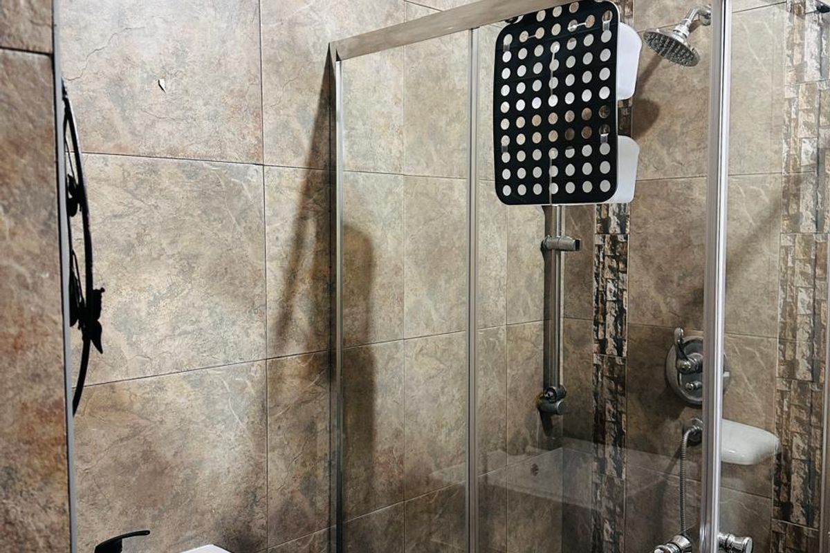 A compact bathroom featuring a modern vessel sink with a black faucet and a glass-enclosed shower with stone-look wall tiling.