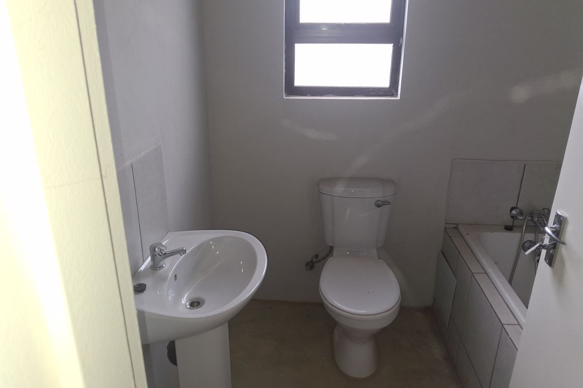 A compact bathroom featuring a pedestal basin, standard toilet, and a bathtub with partially completed tiling, awaiting final finishes.