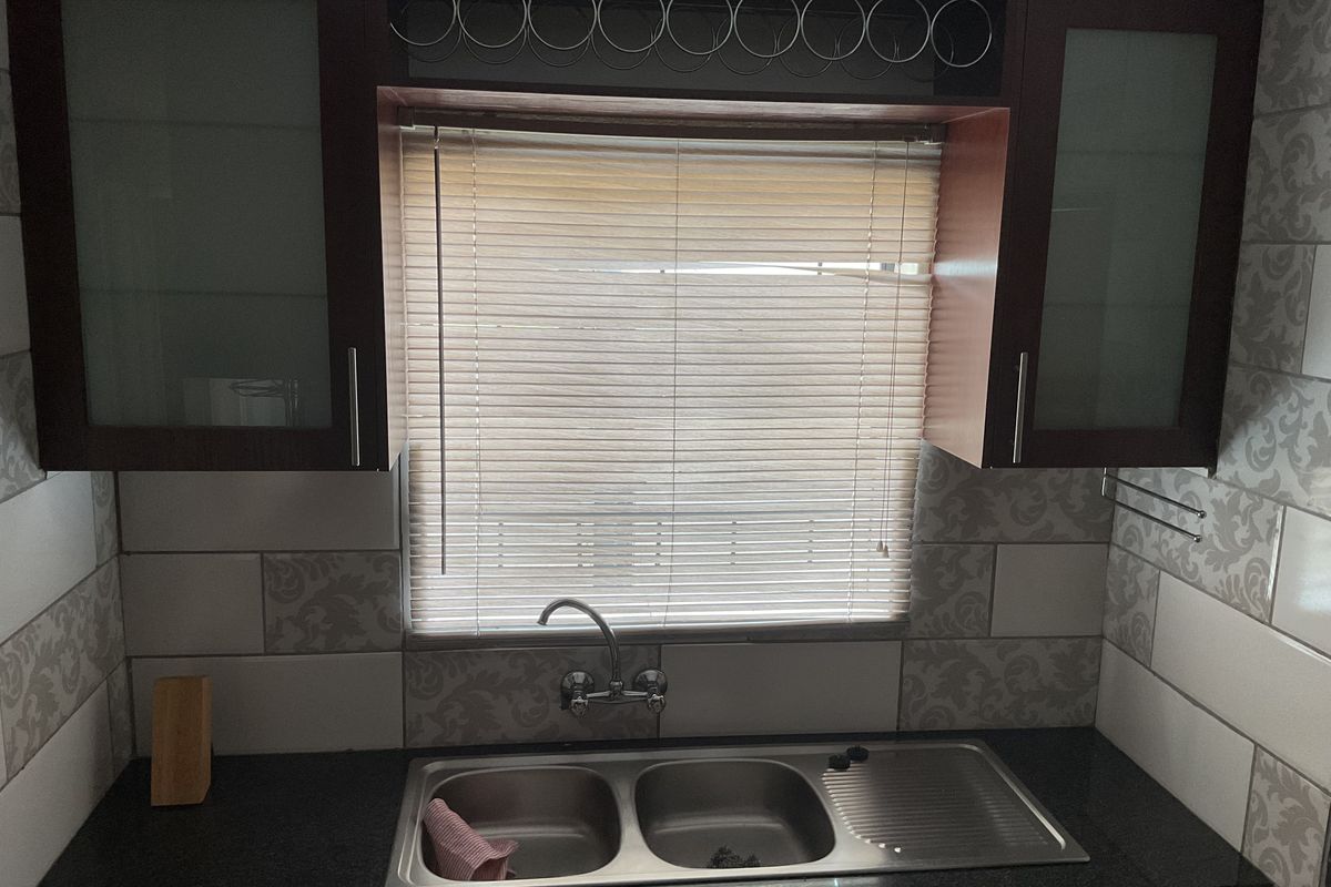 A functional kitchen sink area featuring dark cabinetry, a double-basin stainless steel sink, and decorative patterned wall tiling.