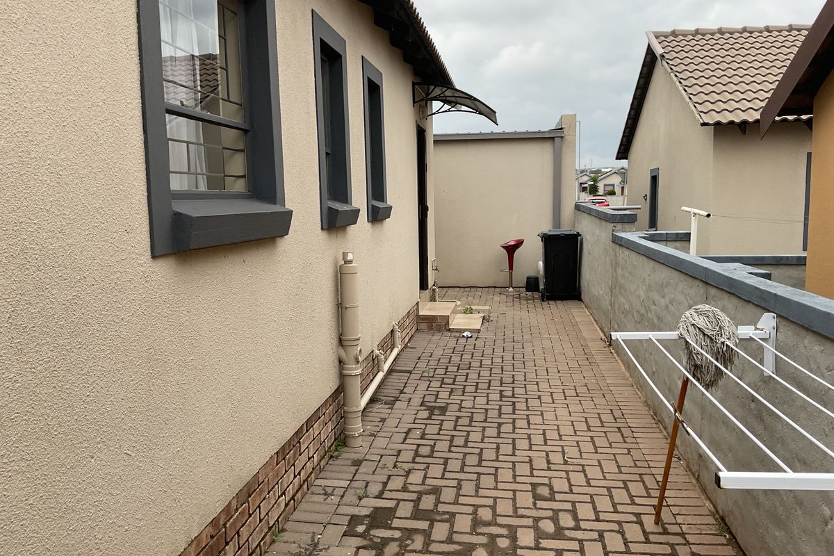 A paved side exterior area featuring a brick-base wall, security window bars, and a small entrance awning.