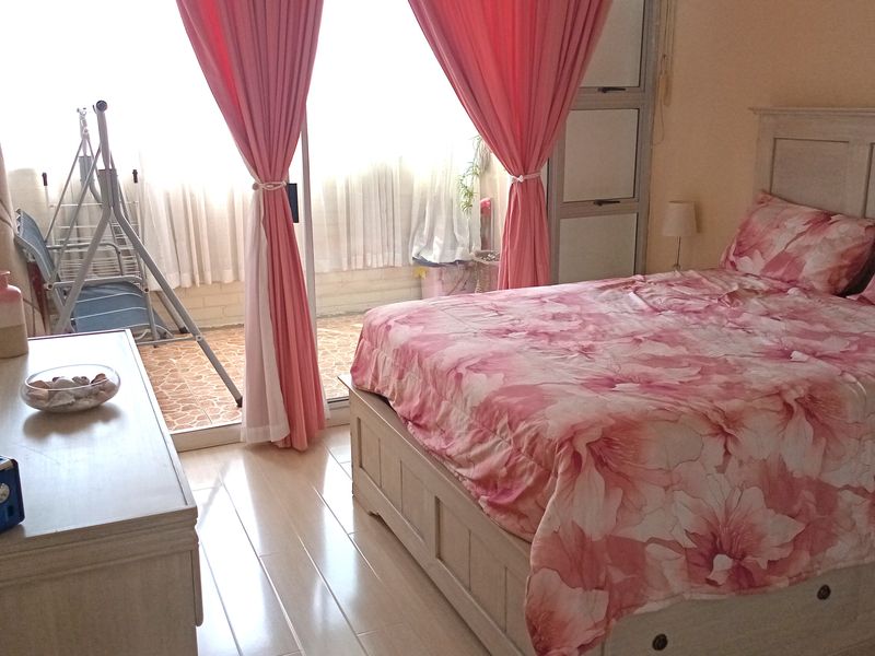 A well-lit bedroom featuring laminate flooring, built-in cupboards, and sliding glass doors that provide direct access to an adjoining balcony.