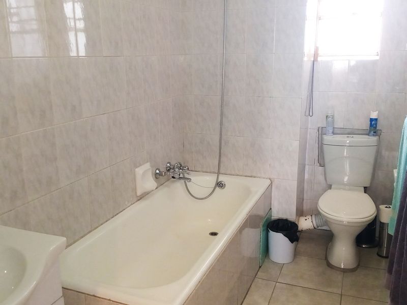 A functional bathroom featuring a bathtub with shower mixer, a pedestal basin, and a standard toilet with tiled walls and flooring.