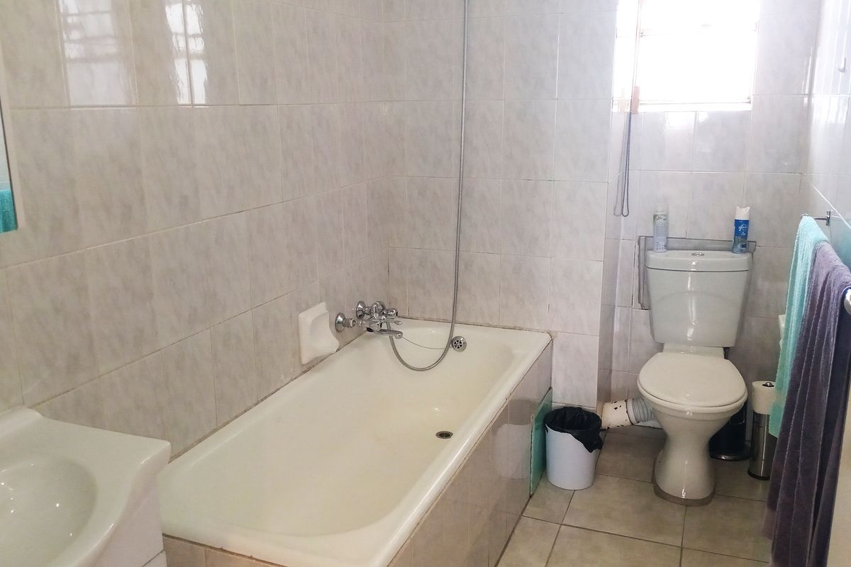 A functional bathroom featuring a bathtub with shower mixer, a pedestal basin, and a standard toilet with tiled walls and flooring.