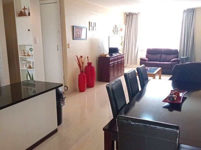 Open-plan living and dining area featuring a kitchen breakfast bar, tiled flooring, and natural light from the window.