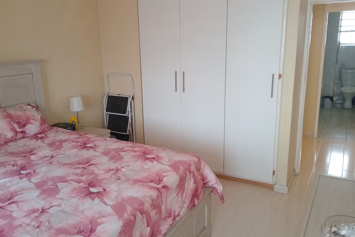 A bedroom featuring built-in wardrobes and light-toned flooring, with an adjacent view into a tiled bathroom.