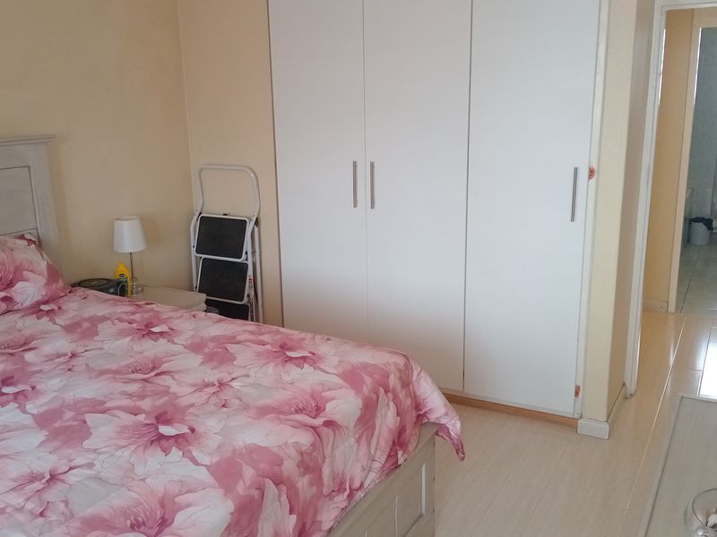 A bedroom featuring built-in wardrobes and light-toned flooring, with an adjacent view into a tiled bathroom.