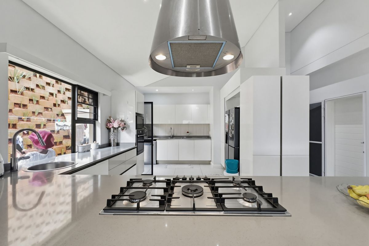 Modern kitchen featuring a central island with a gas hob, stainless steel extractor fan, sleek white cabinetry, and stone countertops.