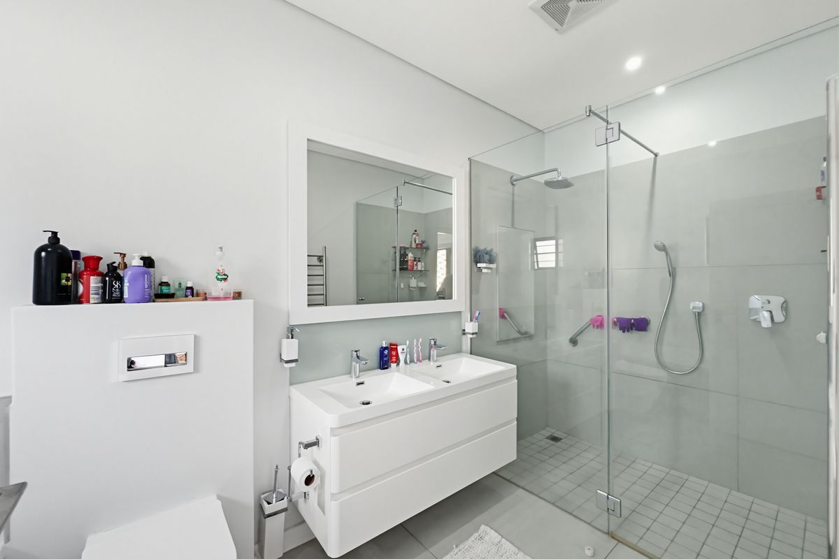 Modern bathroom featuring a double vanity with integrated sinks, a large frameless glass walk-in shower, and a wall-mounted toilet.