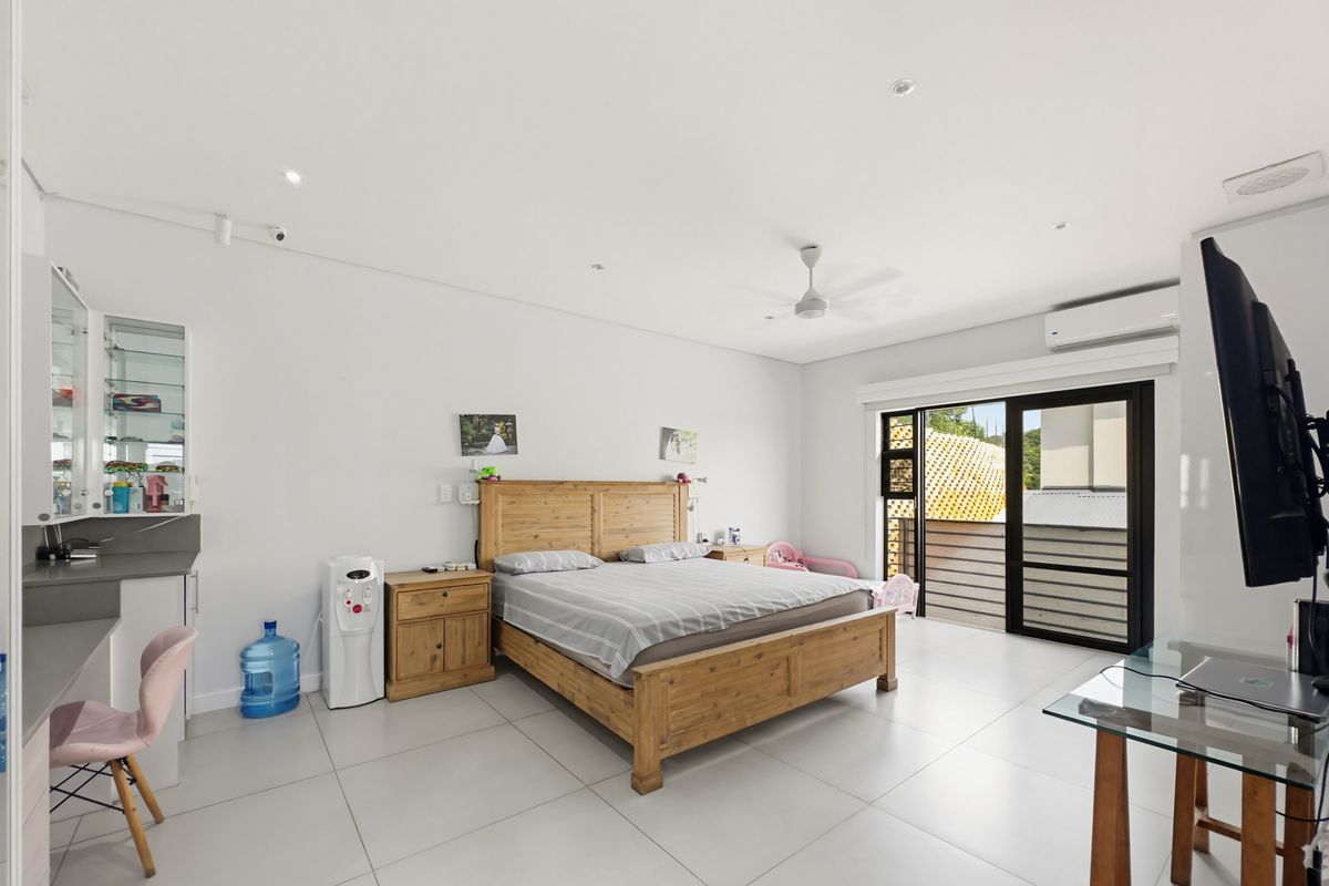 Spacious bedroom featuring large format floor tiles, a ceiling fan, integrated air conditioning unit, and sliding glass doors leading to an outdoor balcony.