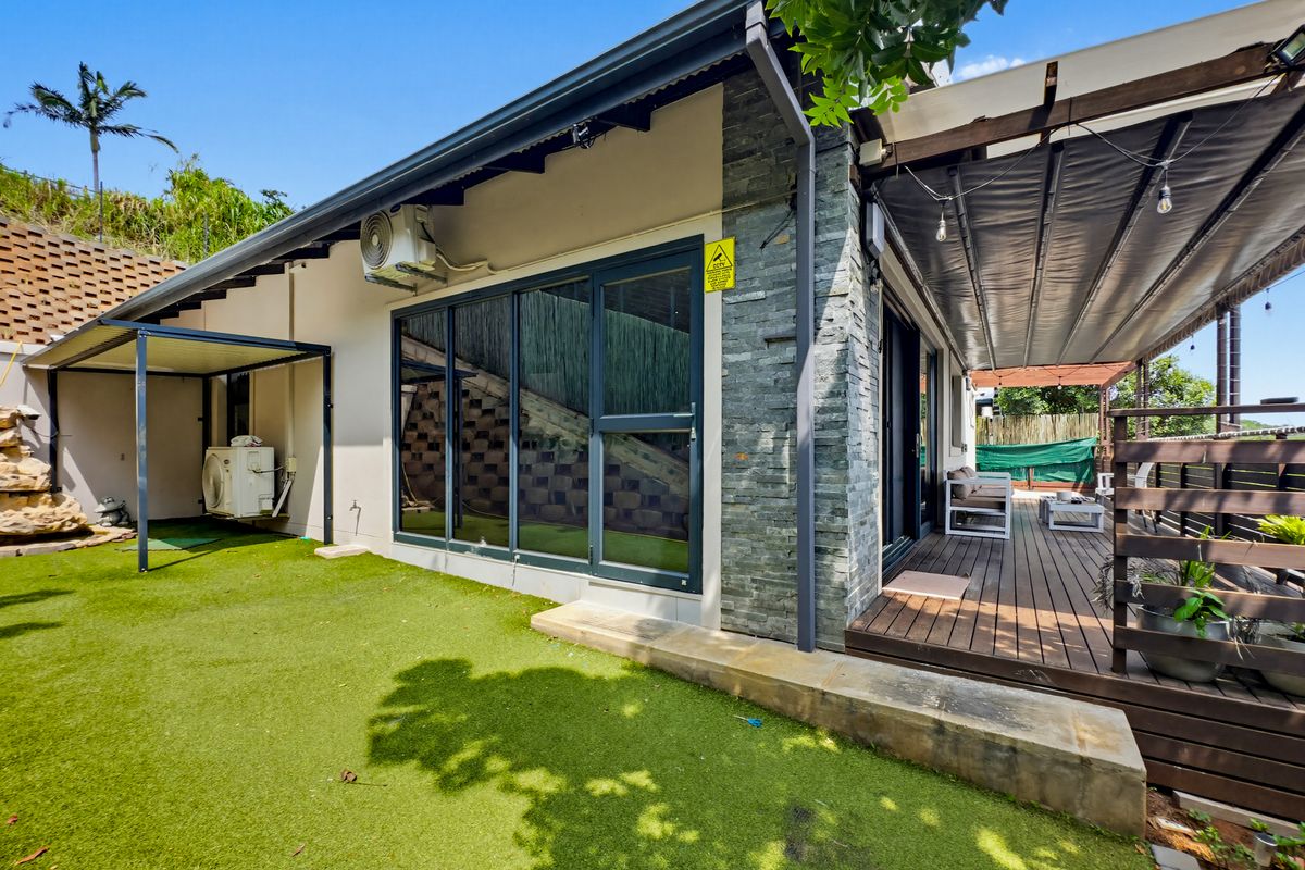 Rear exterior view of the townhouse featuring a timber deck, retractable patio cover, artificial lawn, and stone-clad feature wall.