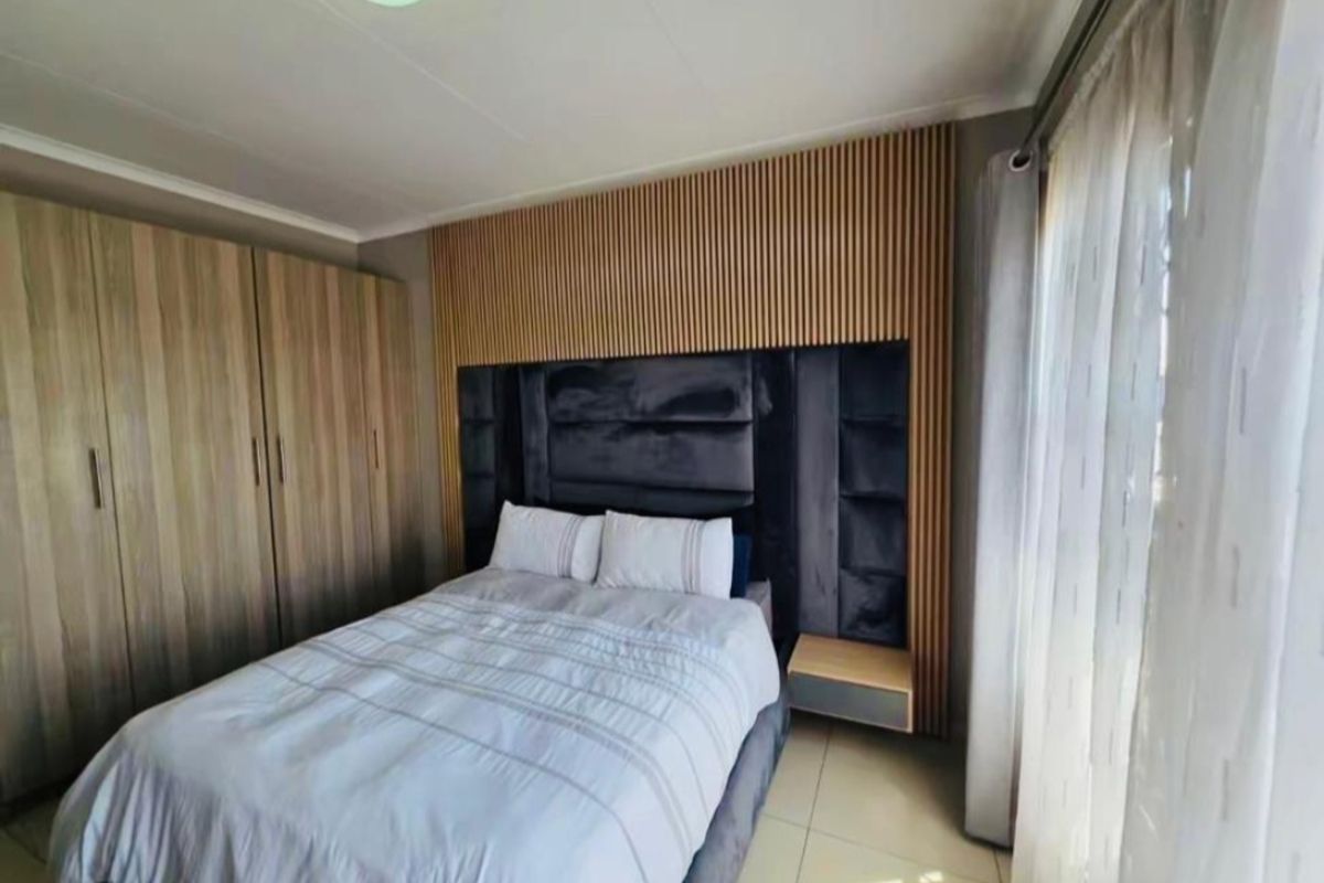 A well-maintained bedroom featuring built-in wooden wardrobes and a modern slatted wood feature wall behind the bed.