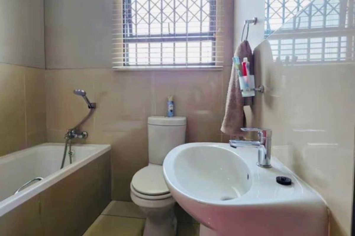 A functional bathroom featuring a pedestal basin, a standard bathtub with shower mixer, and a toilet, finished with neutral wall and floor tiles.