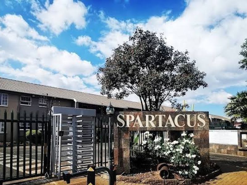 Front entrance view of the Spartacus townhouse complex featuring a secure gated access point, stone-clad signage, and paved driveway.