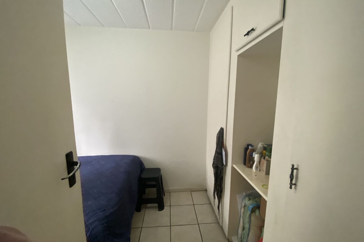 A compact bedroom featuring tiled flooring and a built-in cupboard with open shelving.