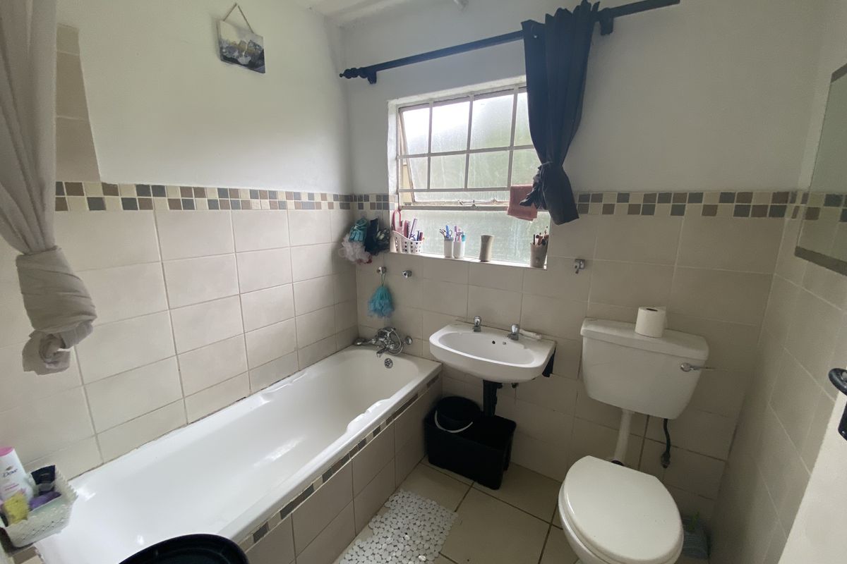 A functional bathroom featuring a bathtub, pedestal basin, and toilet with neutral wall and floor tiling, offering potential for modernization.