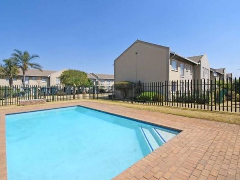 A communal swimming pool area featuring brick paving and secure metal perimeter fencing, set within a well-maintained townhouse complex.