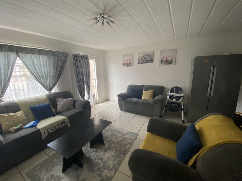 A living room featuring tiled flooring, a ceiling light fixture, and a sliding glass door providing access to the exterior.