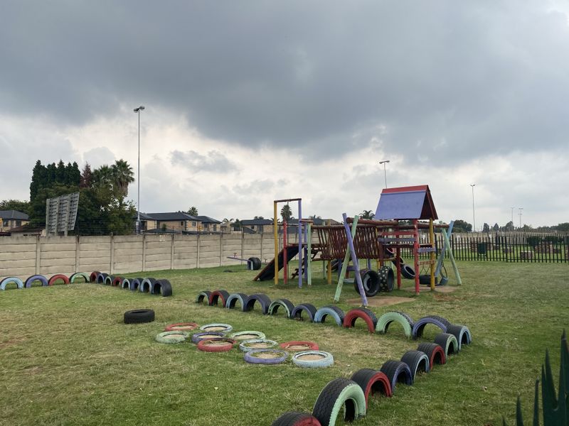 Communal garden area featuring a playground with climbing structures and tire borders, enclosed by perimeter walls and metal fencing.