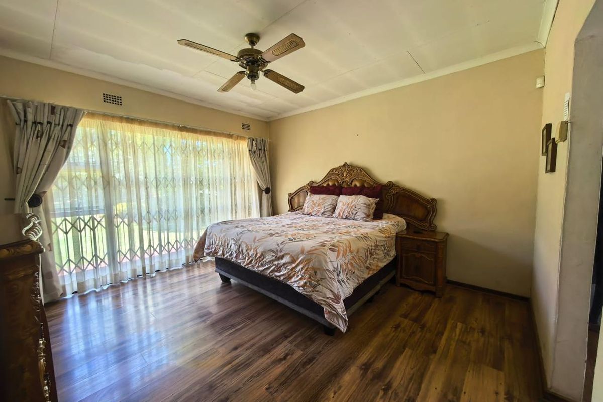 Spacious bedroom featuring wood-look laminate flooring, a ceiling fan, and large sliding glass doors with security gates leading to the exterior.