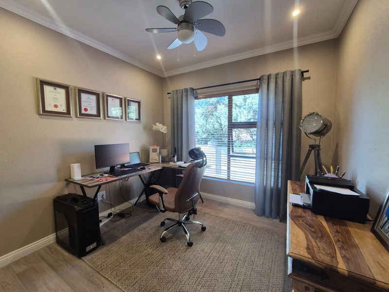 A well-maintained home office featuring laminate flooring, recessed lighting, a ceiling fan, and a large window with blinds providing natural light.
