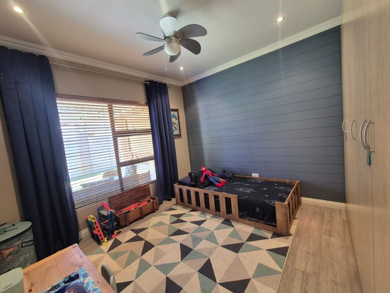 A well-maintained bedroom featuring a dark blue shiplap accent wall, built-in cupboards, laminate flooring, and a ceiling fan.
