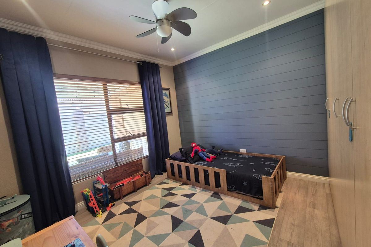 A well-maintained bedroom featuring a dark blue shiplap accent wall, built-in cupboards, laminate flooring, and a ceiling fan.