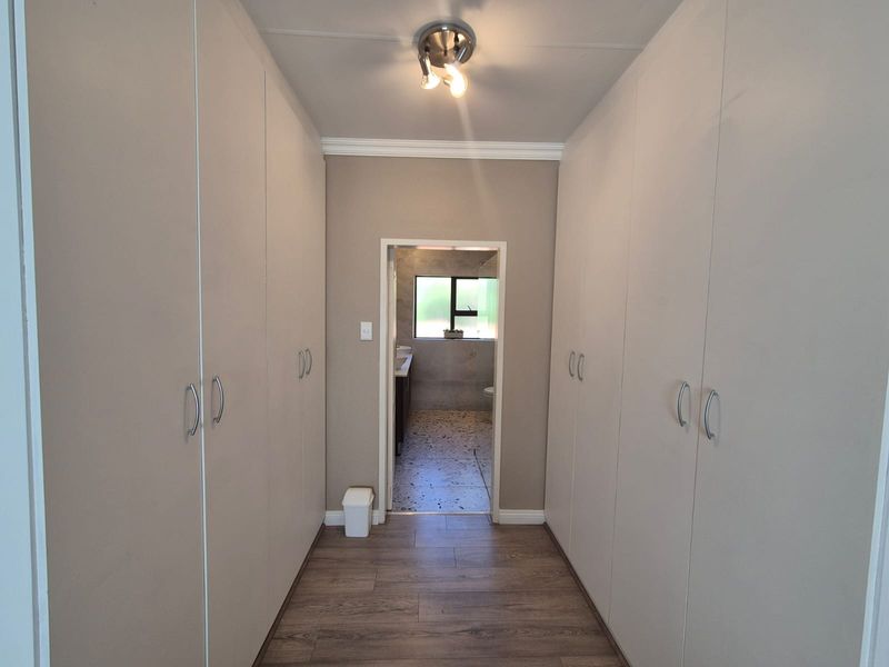 A clean, well-maintained hallway featuring extensive built-in cupboard storage and laminate flooring, leading directly into an adjacent bathroom.